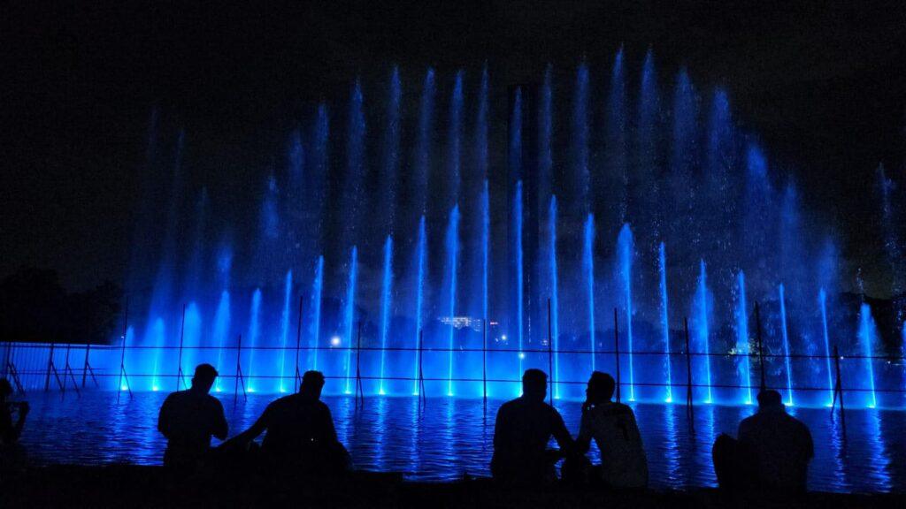 Blue lit water fountain show with silhouettes of people sat down