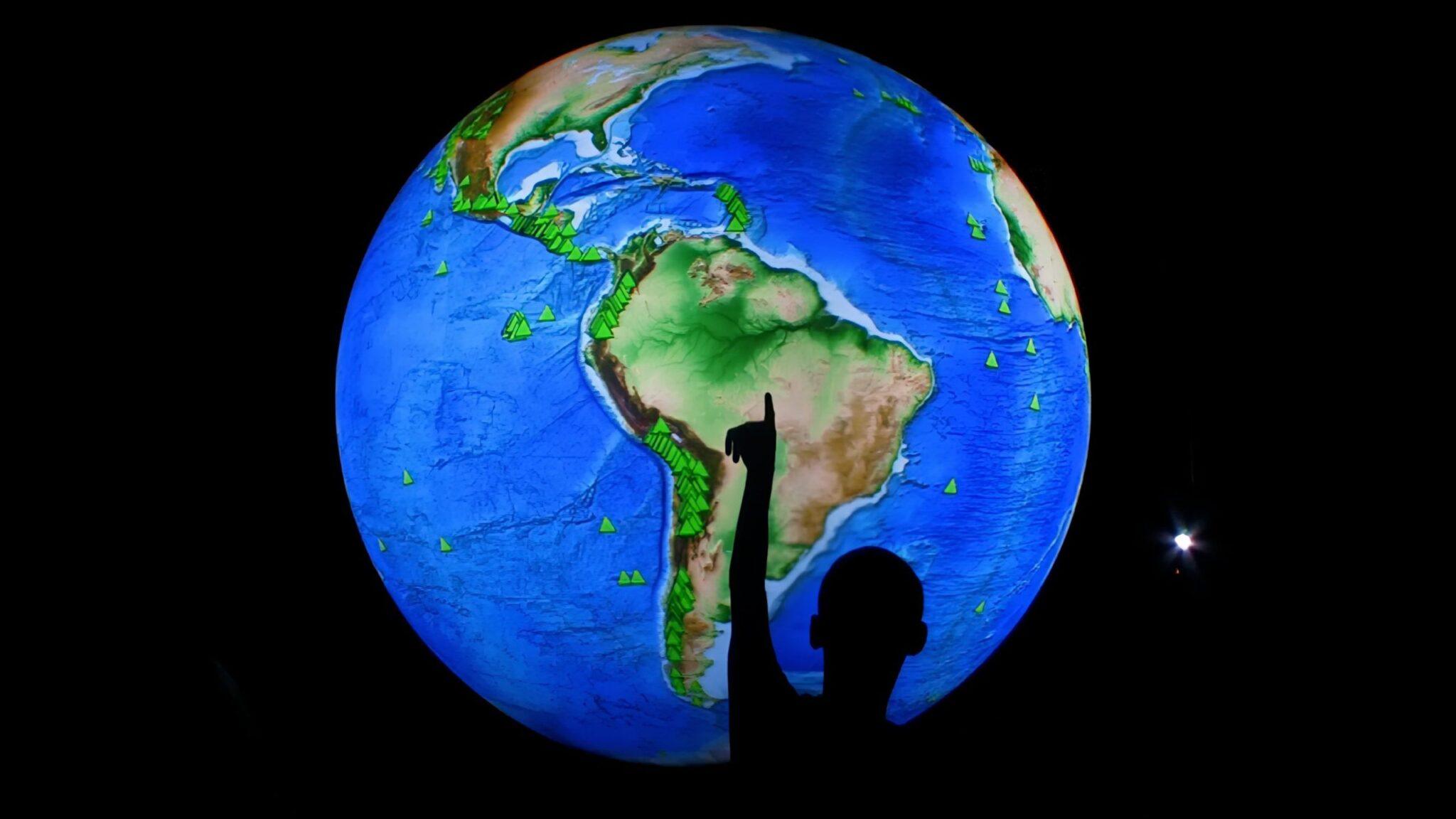 Silhouette of person pointing at a globe holograph